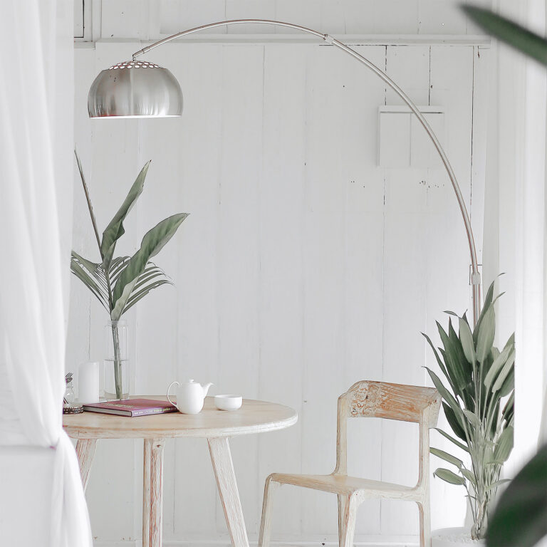 Minimalistisch eingerichtete Sitzecke mit runder Holzbank, Bogenlampe und Pflanzen in hellem Raum
