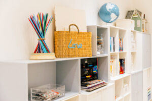 Weißes Regal mit Deko, Büchern, Bastelmaterial, Globus und einem Puppenhaus.