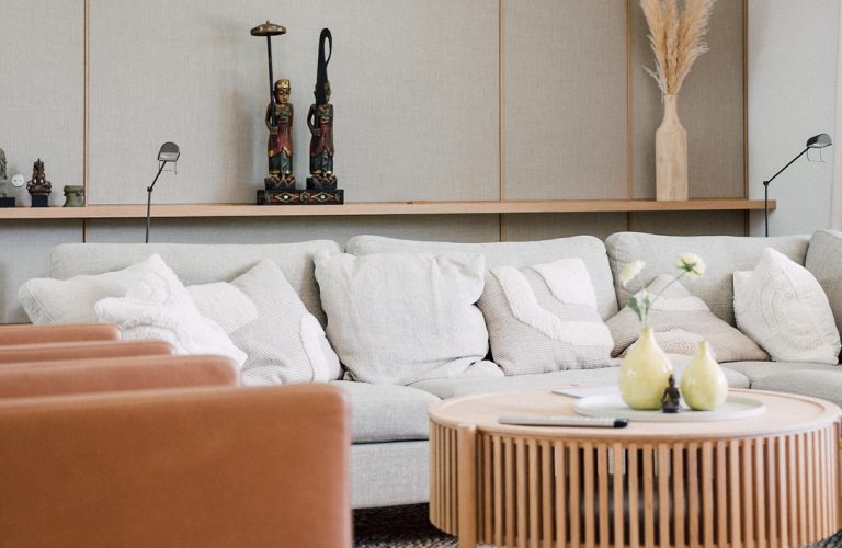 Modernes Wohnzimmer mit hellgrauem Sofa, Kissen, Dekofiguren, rundem Holztisch und stilvoller Wandgestaltung.
